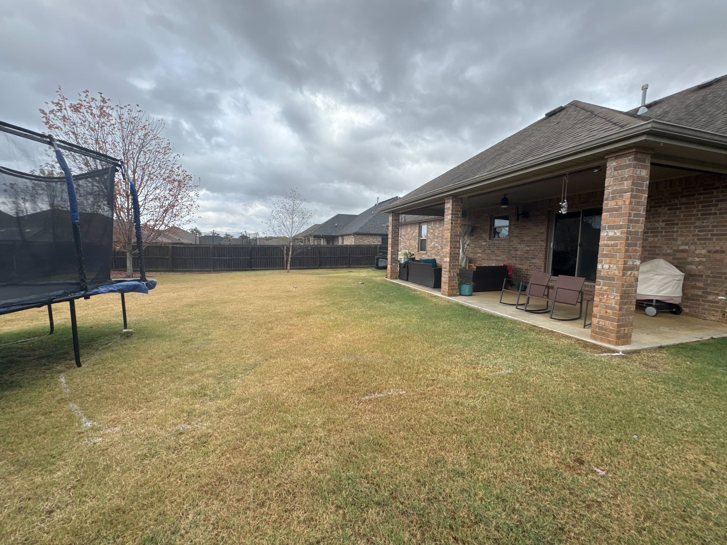Brick home's small covered porch and brown lawn with a trampoline before the remodel.