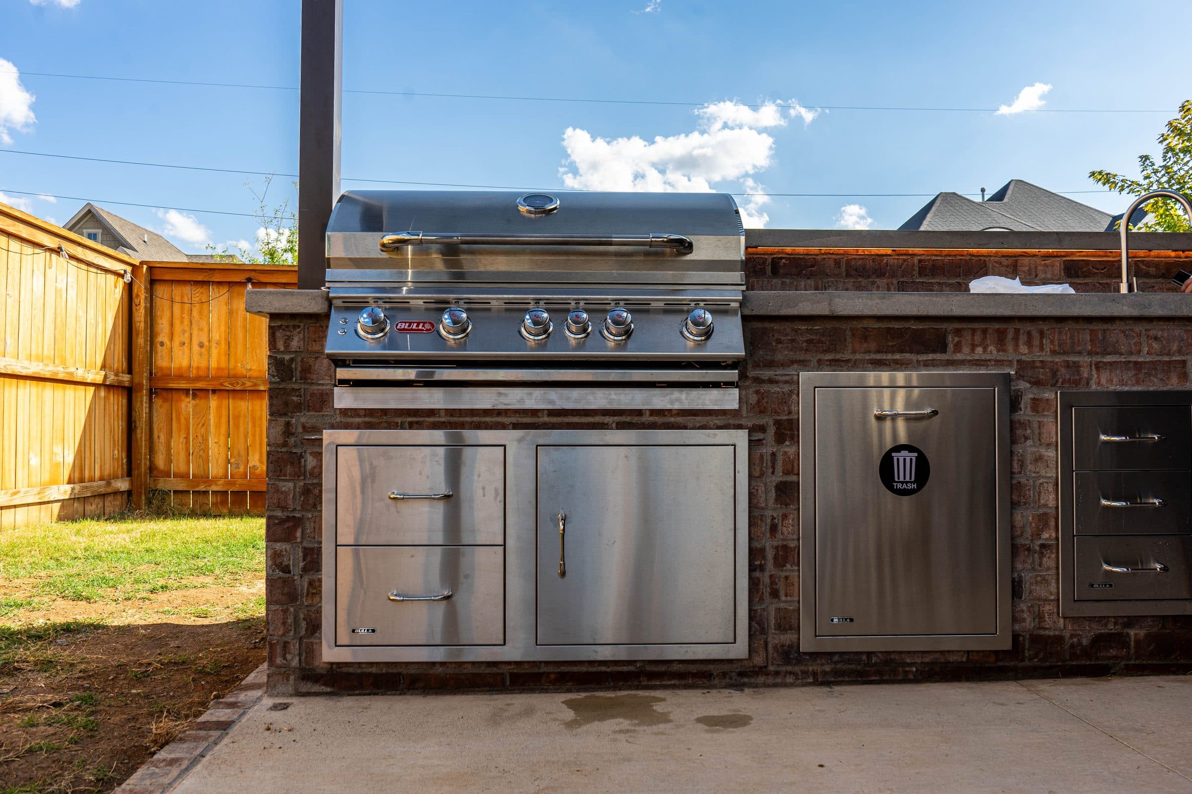 Full brick outdoor kitchen run with a built-in stainless grill, storage doors, drawers and trash pull-out.