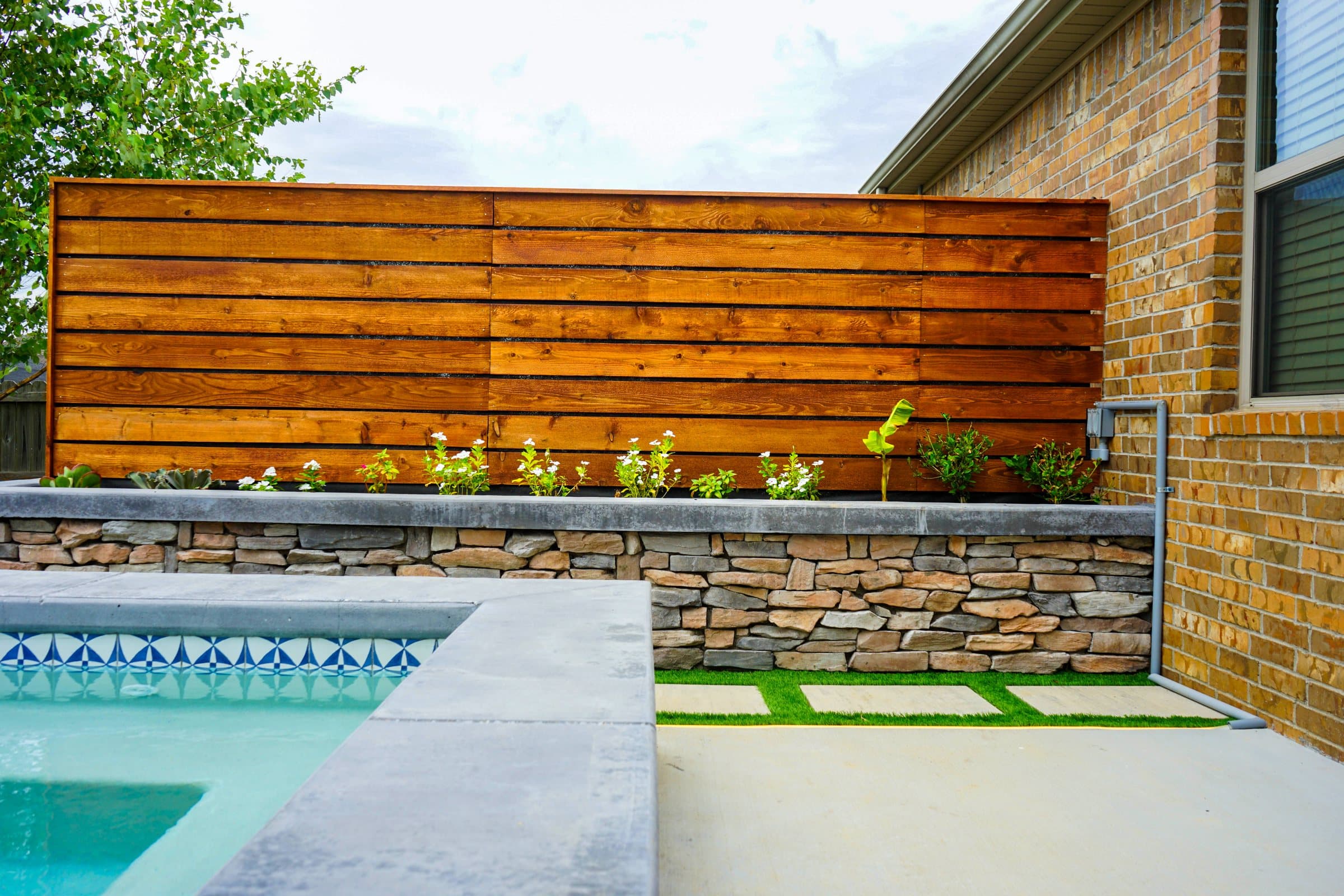 Stained cedar screen wall over a stone planter beside the spa's gray coping.