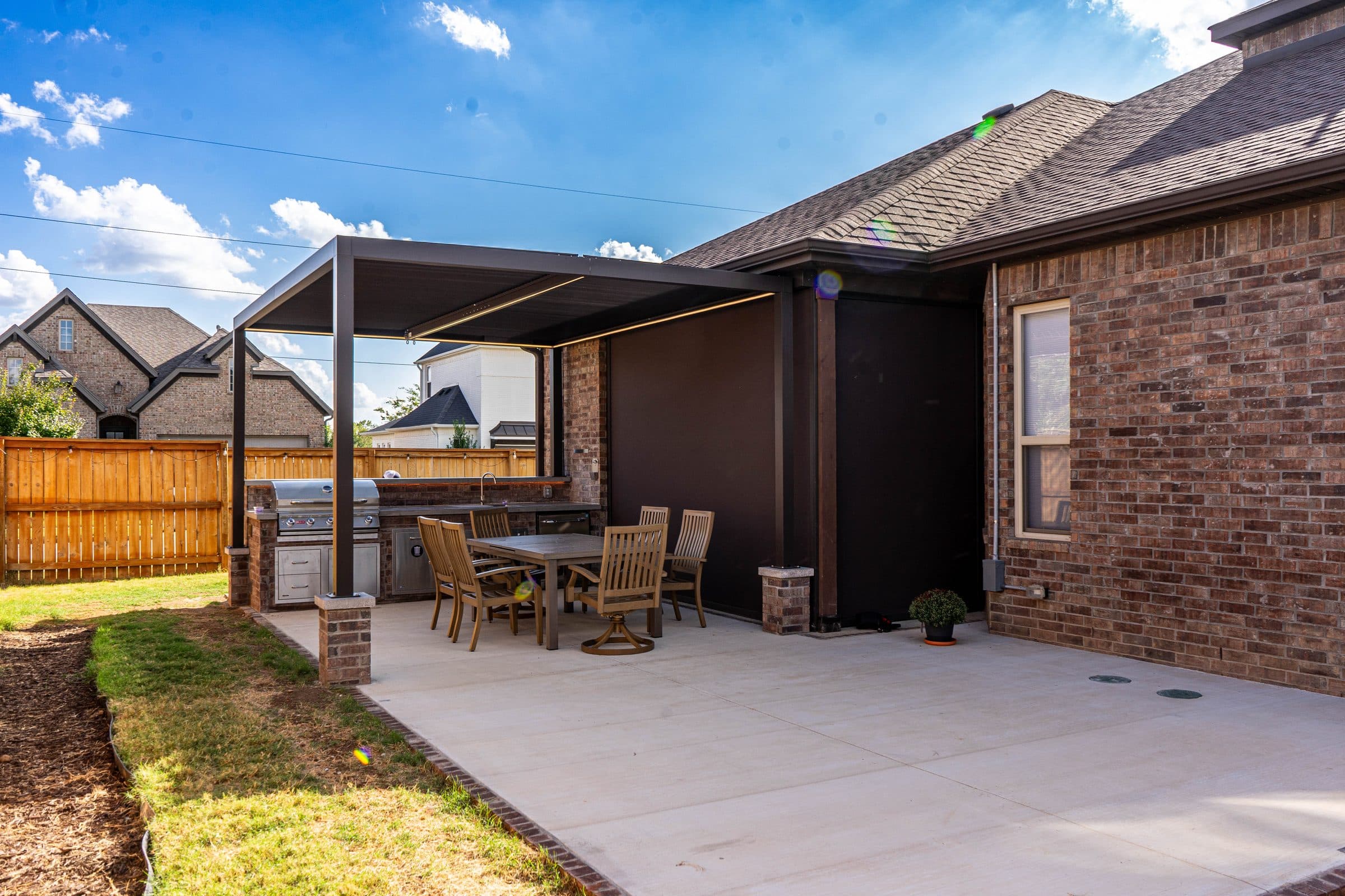 New concrete patio running off a brick home to a louvered pergola and outdoor kitchen.