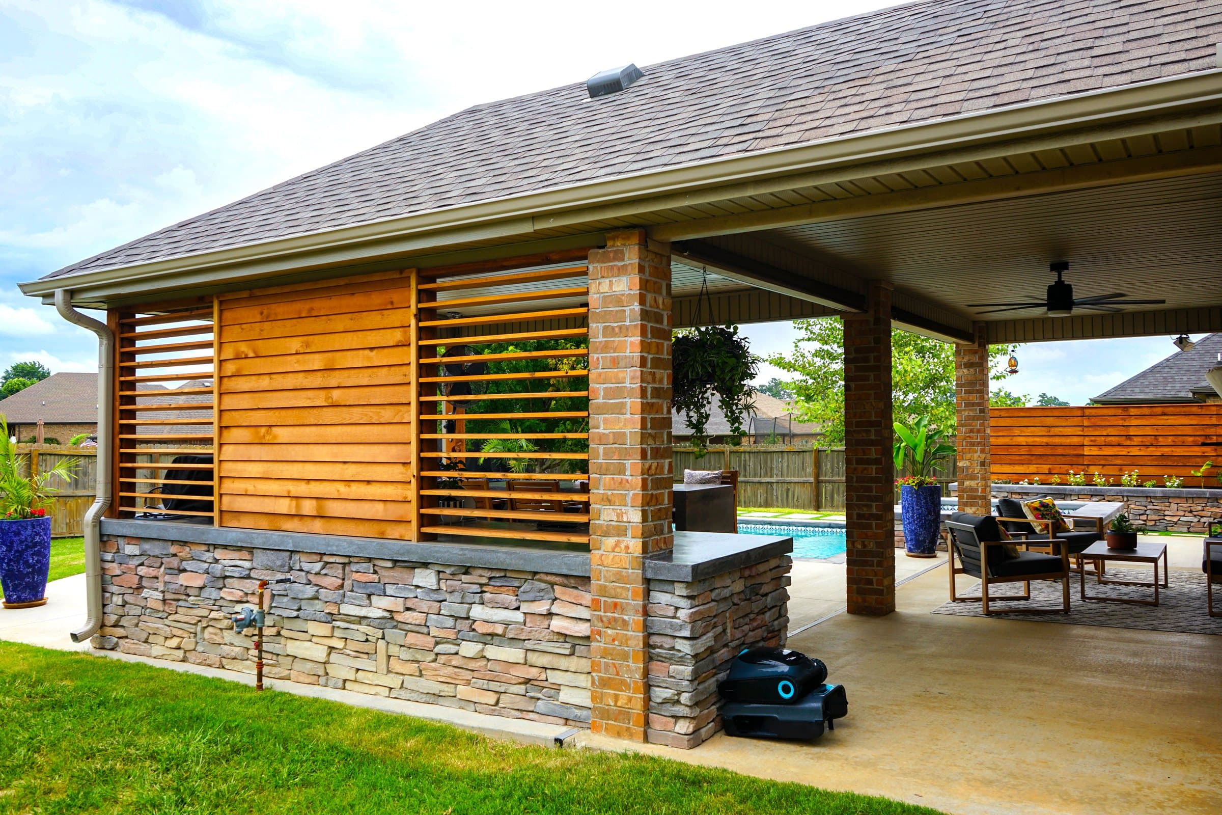 Covered patio with cedar slat screen panels over a stone knee wall and brick columns.
