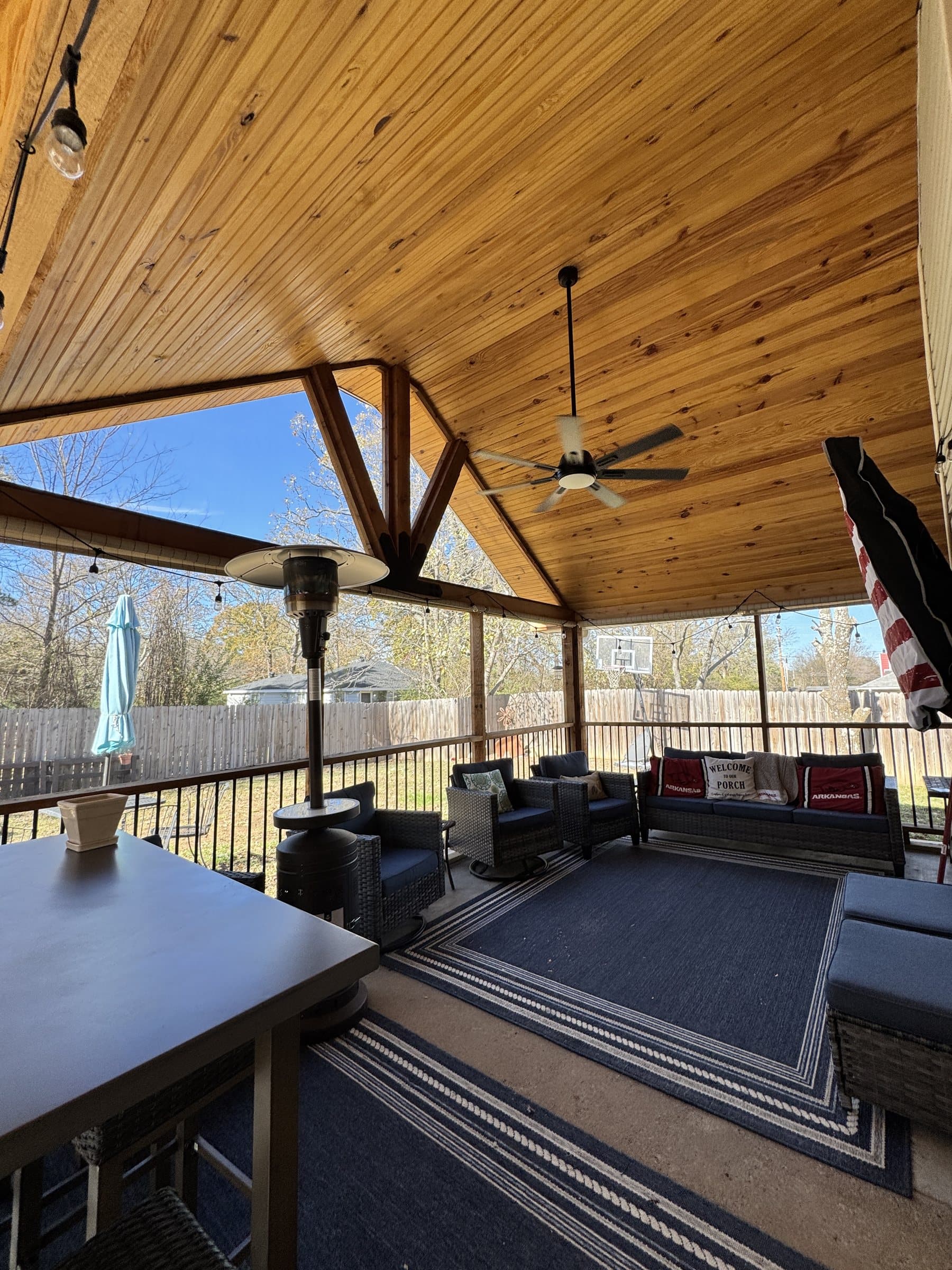 Covered deck with a gabled tongue-and-groove wood ceiling, ceiling fan and wicker seating.