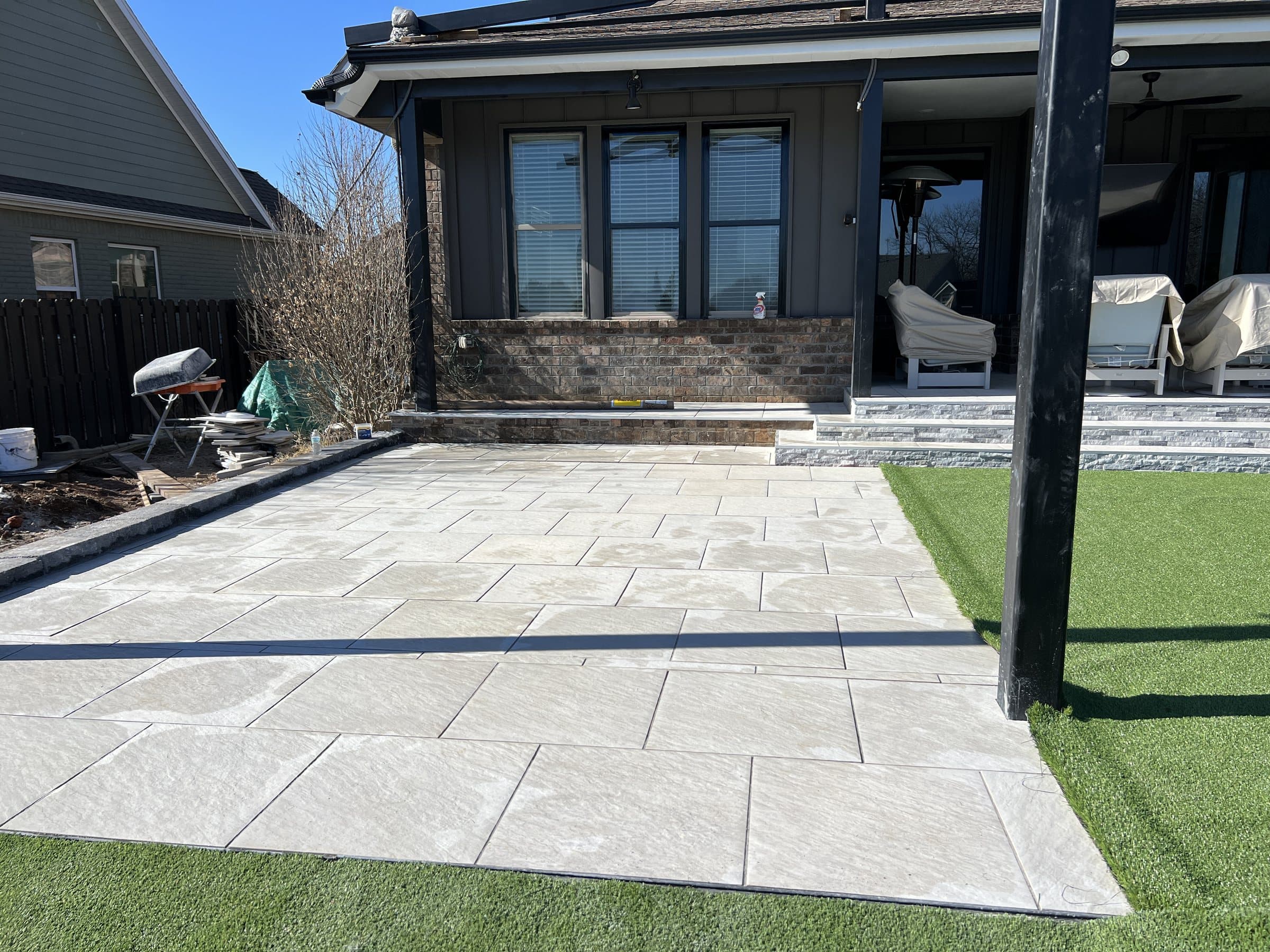 A light gray large-format paver patio meets artificial turf at a covered back porch.