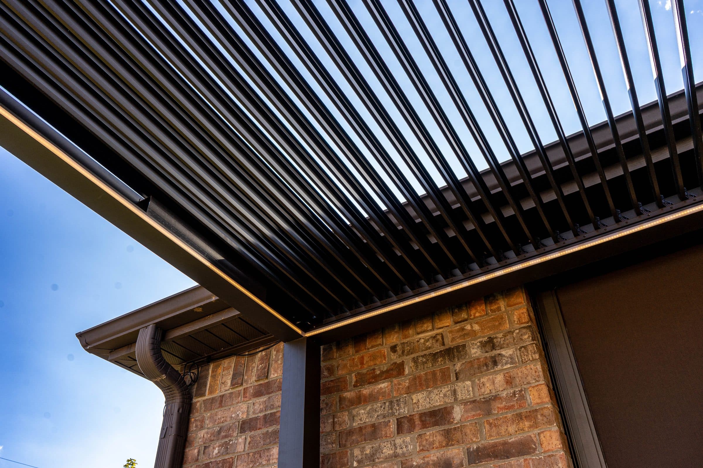 Louvered pergola roof with lighting, tied into the brick wall and roofline of the house.