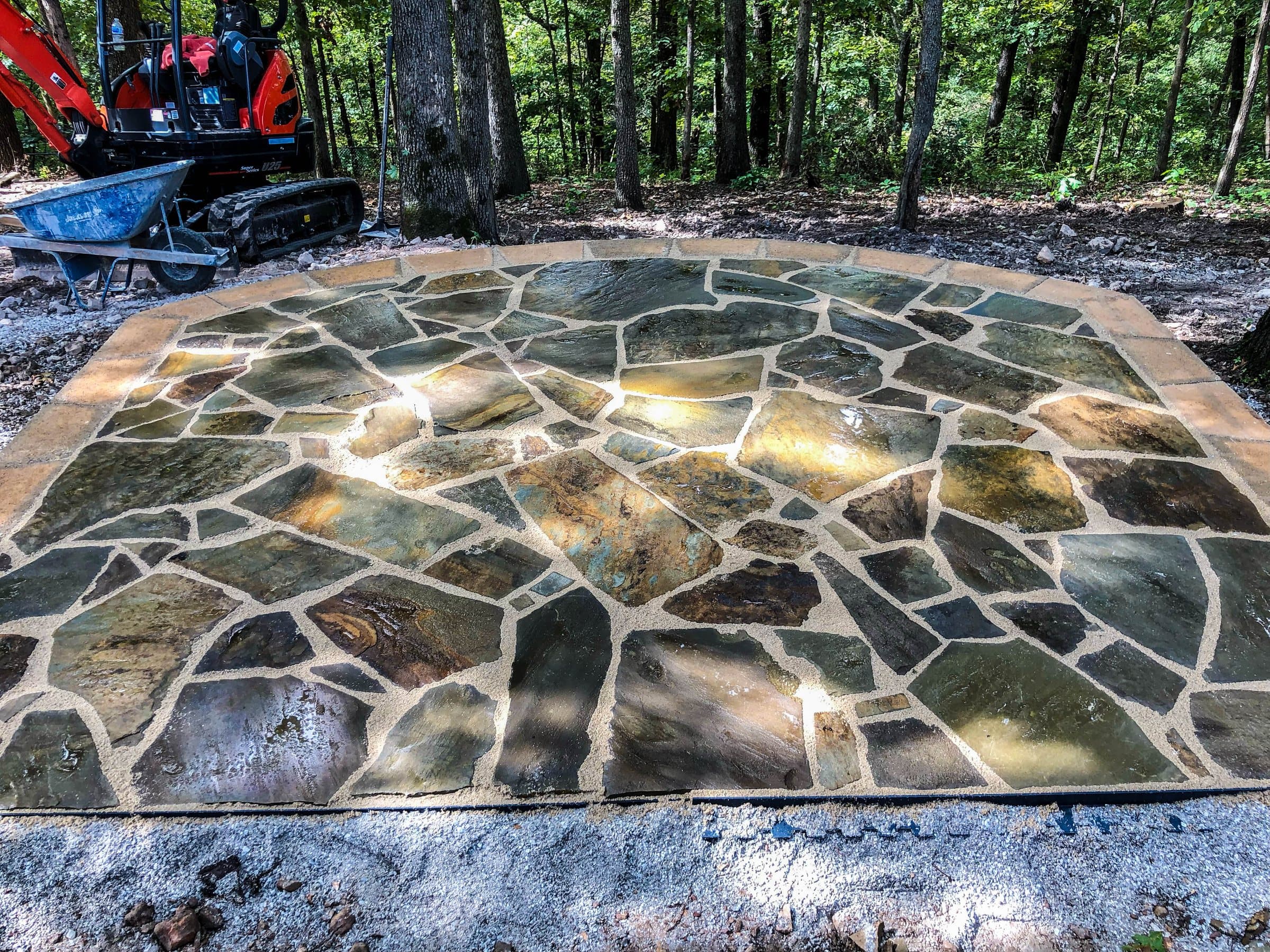A mortared multicolor flagstone patio with a sandstone border in a wooded yard.