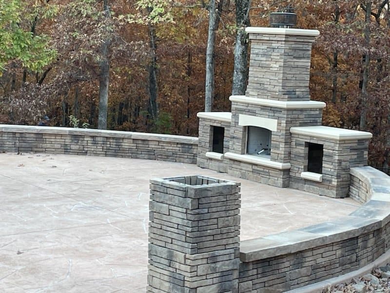 Stone outdoor fireplace with wood boxes and a curved seat wall ending in a stone pillar.
