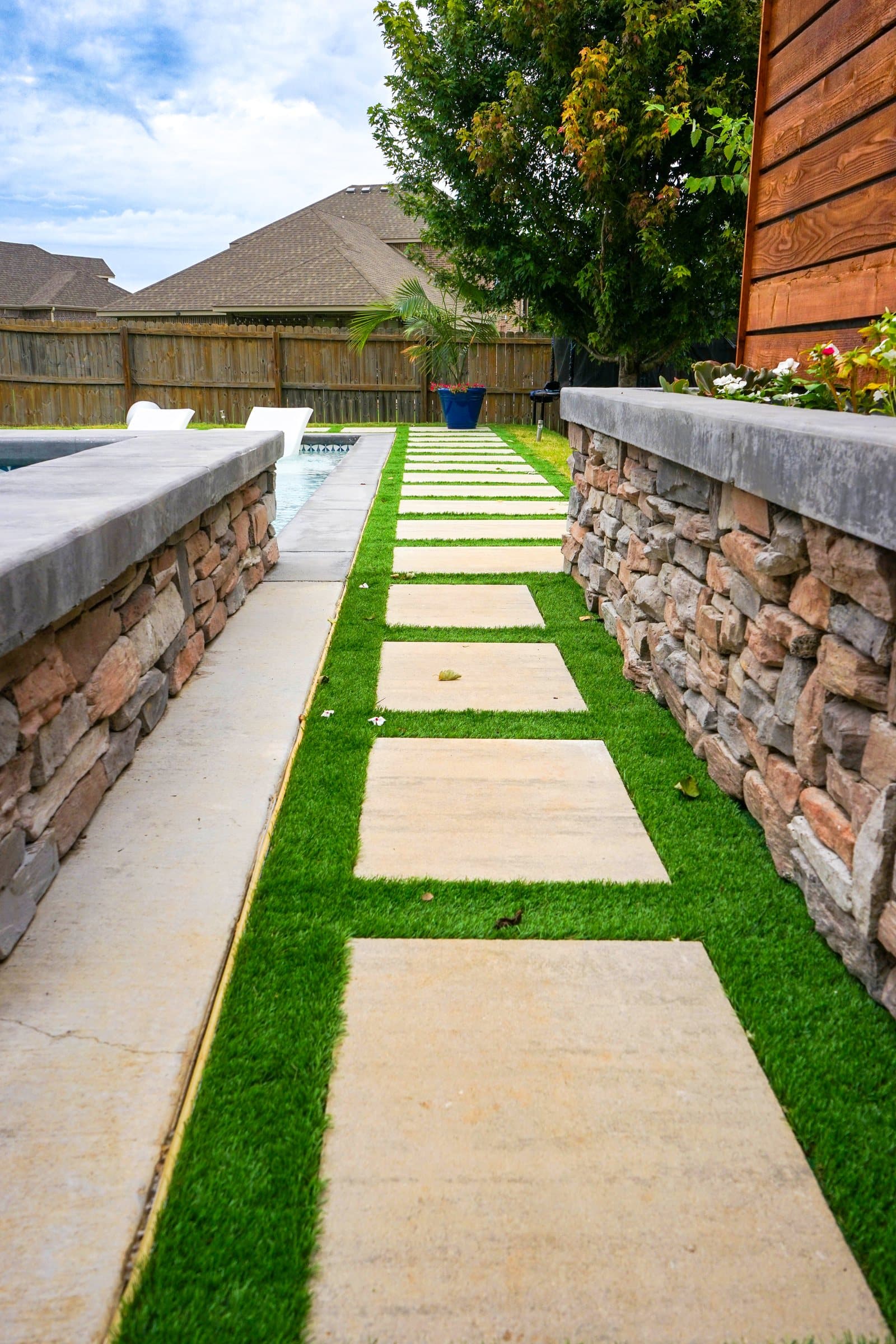Stepping pavers set in turf run between two stacked stone walls toward the pool.