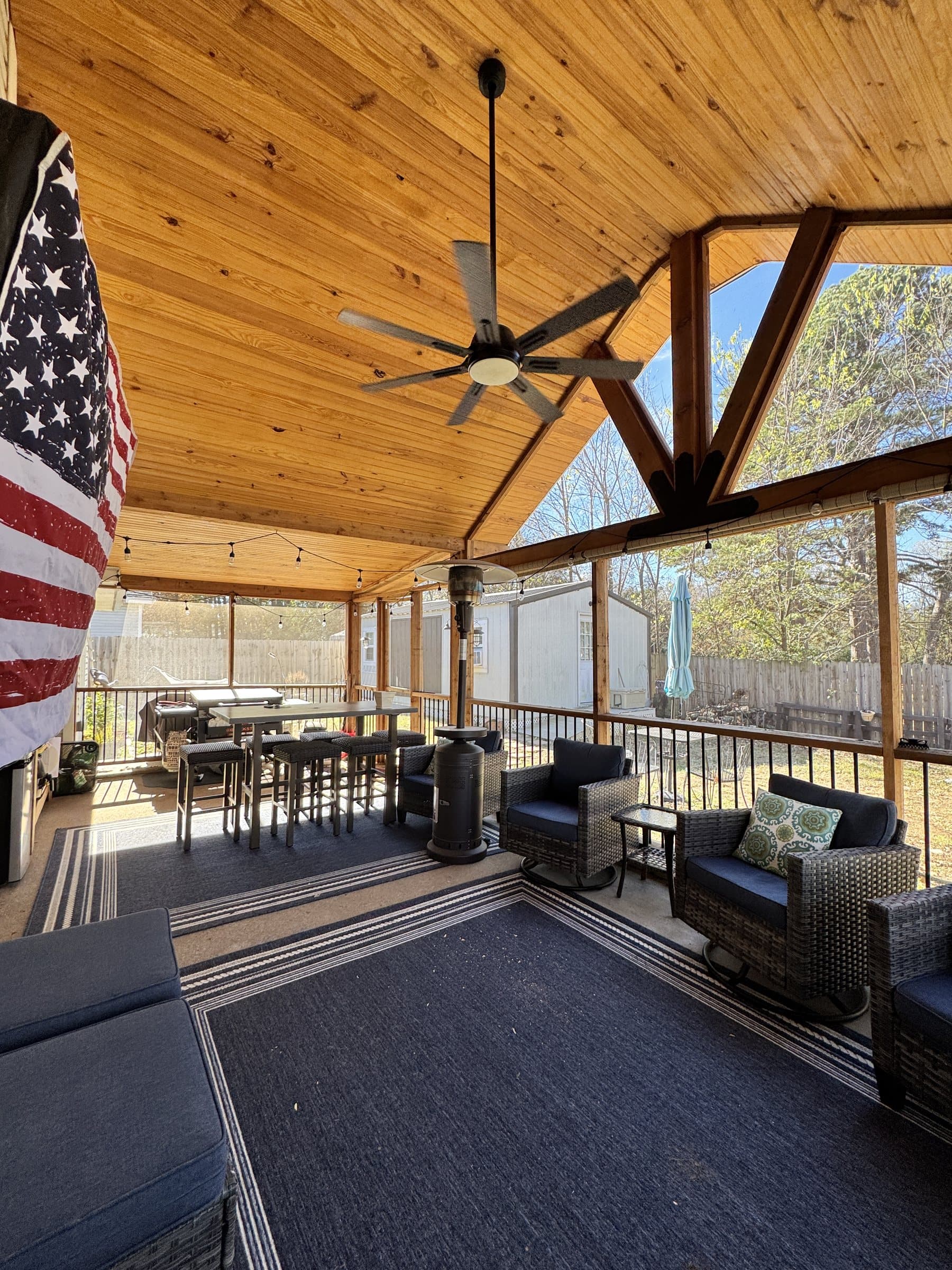 Open-gable pavilion with a warm wood ceiling, timber trusses, fan and outdoor furniture.