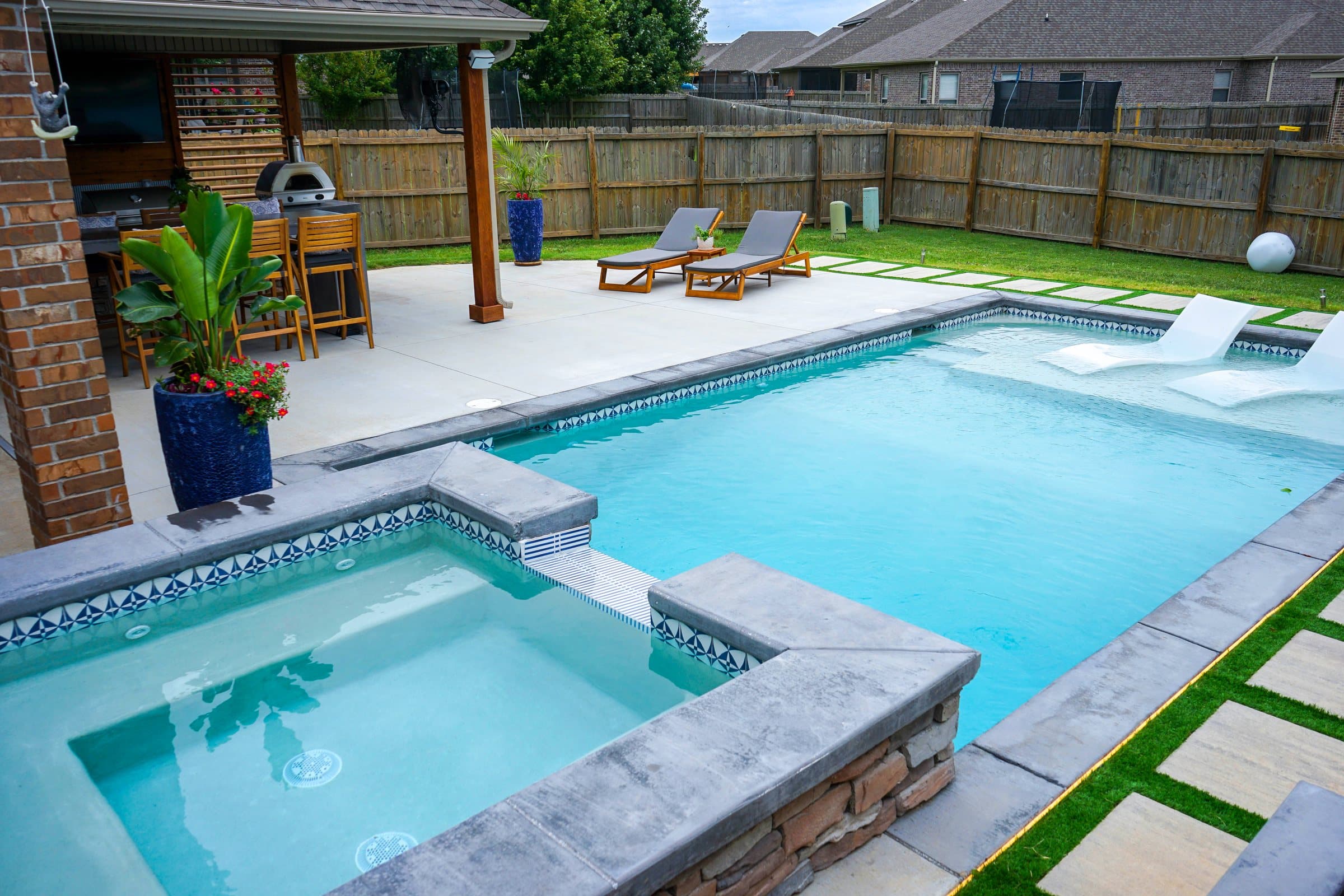 Pool with a raised stone spa and tanning ledge loungers next to a covered patio and bar seating.