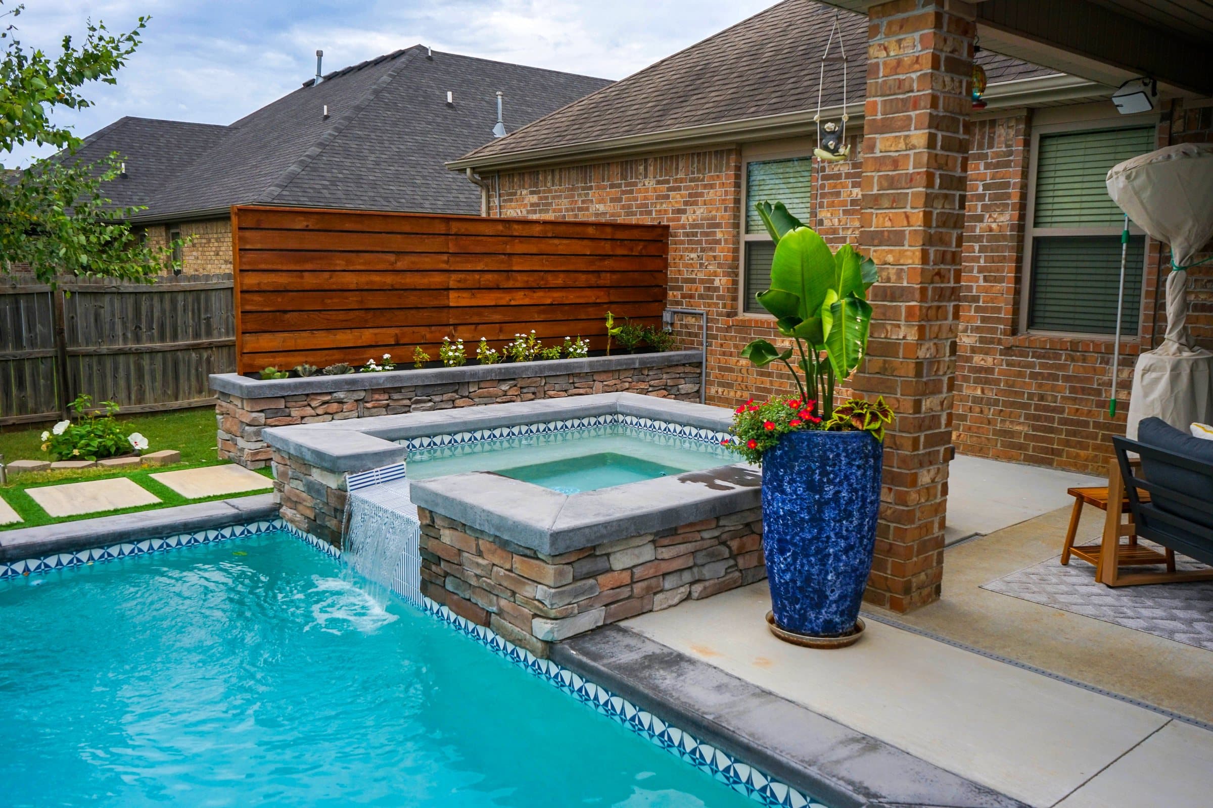 Stacked stone spa spilling into the pool beside a cobalt planter and cedar privacy screen.