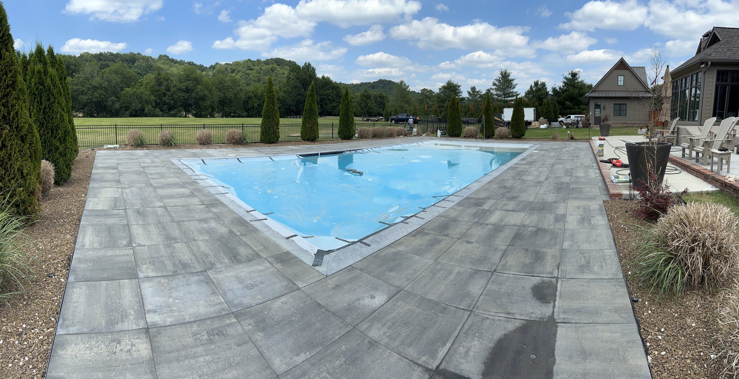 A rectangular pool with blue water surrounded by a gray large-format paver deck and grasses.