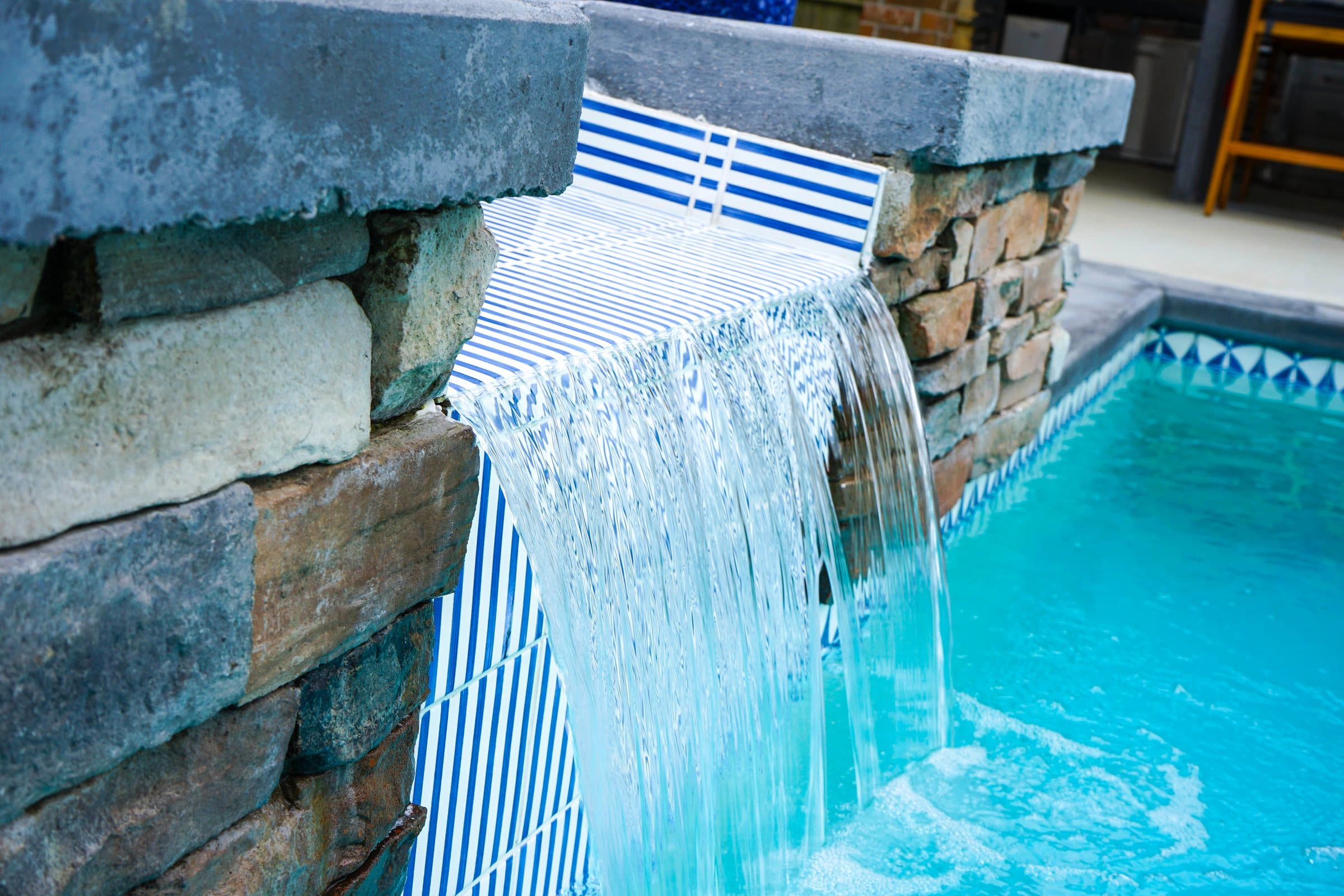 Close-up of a sheer water curtain falling from a stacked stone spa into the pool.