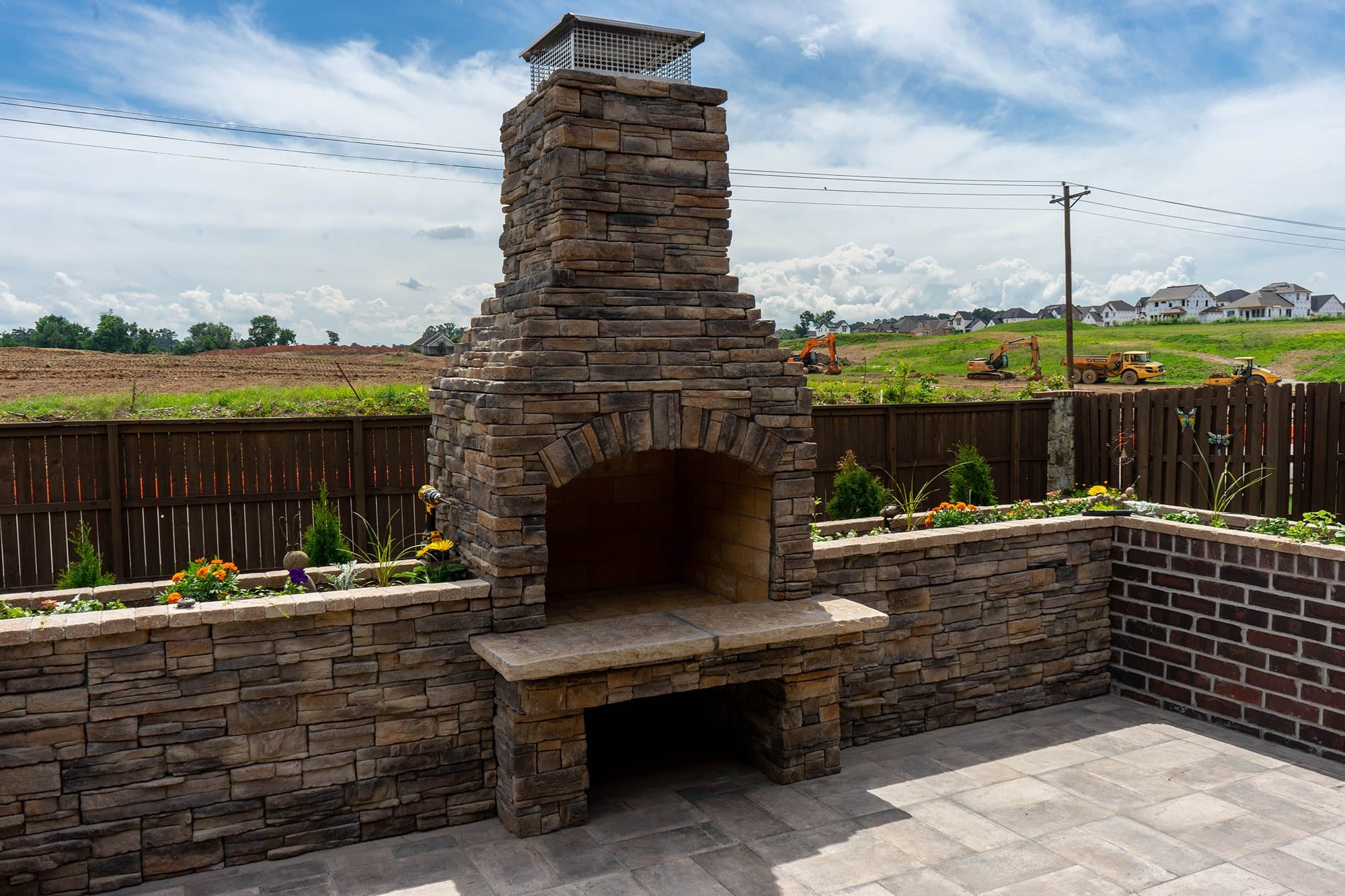 A stacked stone outdoor fireplace with seat walls wraps a gray paver patio.