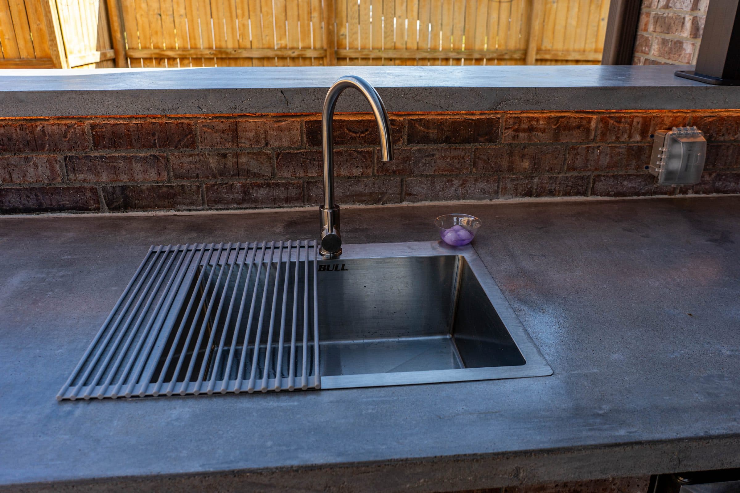 Stainless sink with a roll-up drying rack set into a polished concrete outdoor countertop.