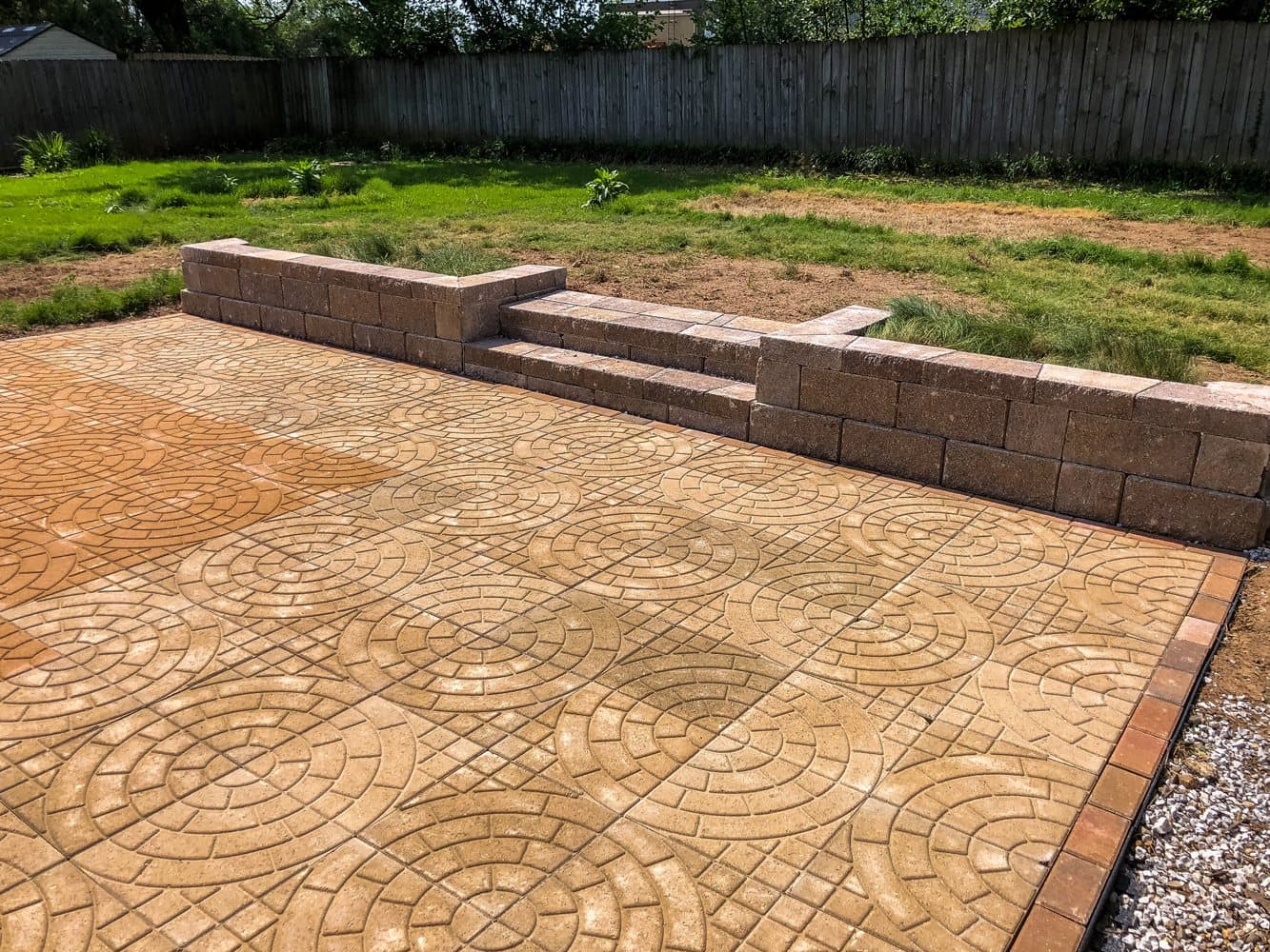 A tan paver patio laid in a circle pattern with a low block seat wall.